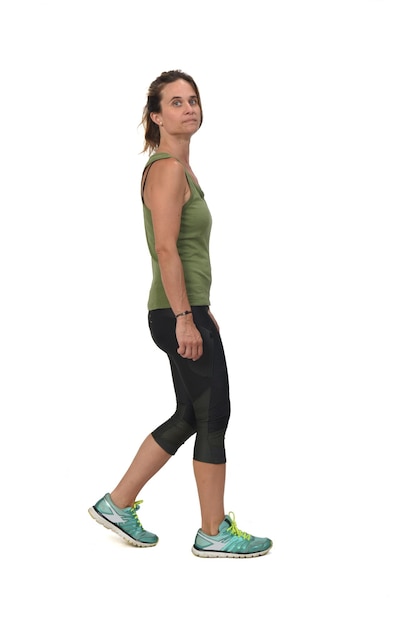 Side view of a woman with sportswear walking and looking at camera on white background