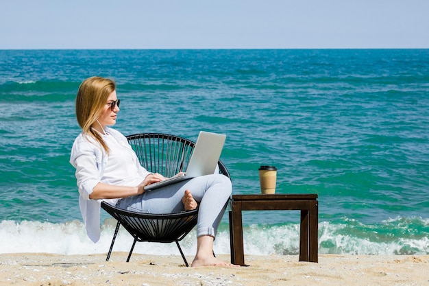 Vista laterale della donna che lavora al computer portatile in spiaggia