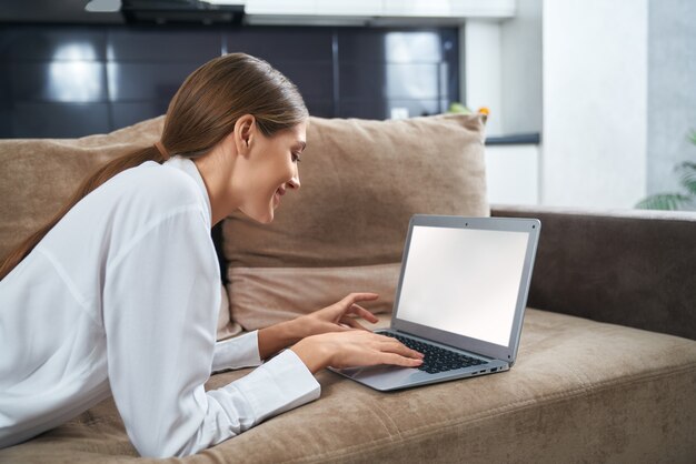 Side view of woman working on laptop while lying on couch