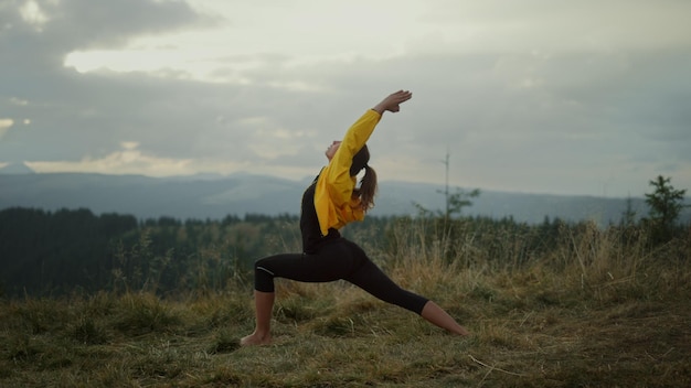 Side view yoga woman doing warrior pose in mountains Flexible girl practicing yoga outdoor Young lady in sportswear performing yoga pose outdoor at sunset