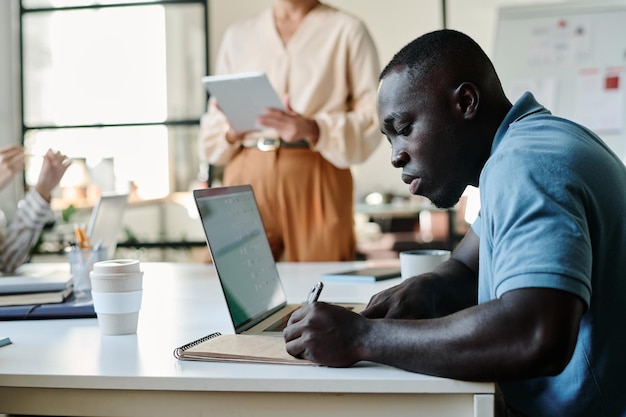 Side view of young african american businessman making notes in notepad