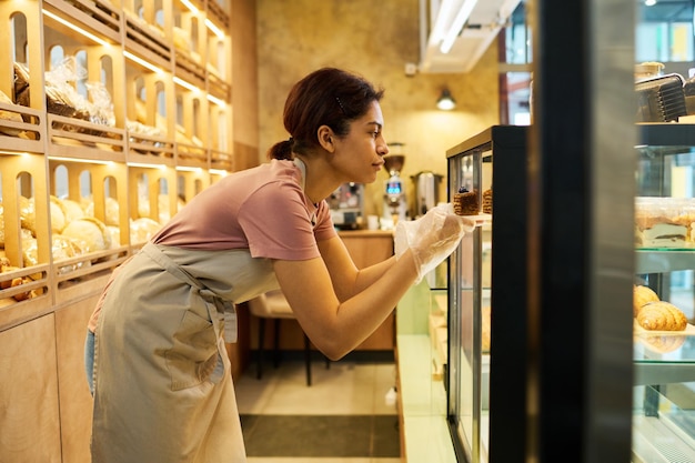 Side view of young African American woman taking dessert out of display