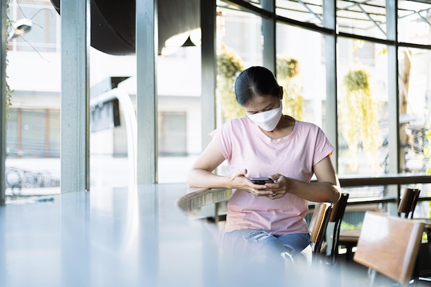 コーヒーショップのデスクでスマートフォンを使用して若いアジアの女性の側面図