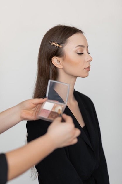 Side view of young attractive woman model waiting for applying eye makeup by makeup artist holding e