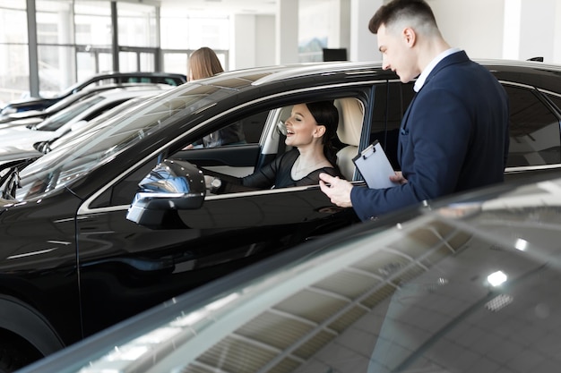 Side view of young beautiful woman sitting inside car and holding hand on steering wheel