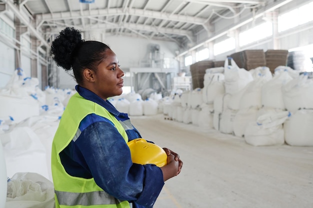 Side view of young black woman in workwear holding yellow safety helmet