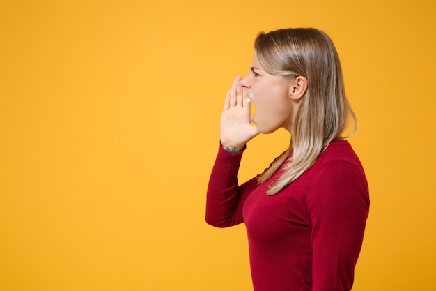 Side view of young blonde woman girl in casual clothes posing isolated on yellow orange background studio portrait. people lifestyle concept. mock up copy space. scream with hand gesture near mouth