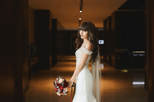 Side view of a young bride in luxurious wedding dress at the interior