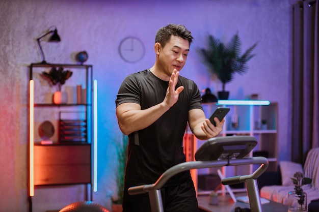 Side view of young confident asian man looking at smartphone during video call while running