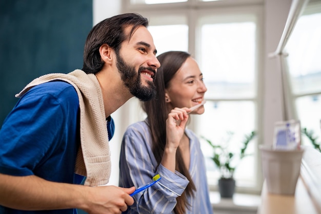 Side view of young couple brushing teeth in front of mirror indoors at home.