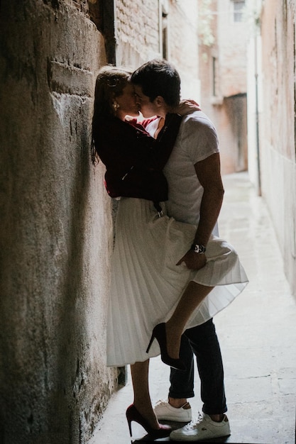 Photo side view of young couple kissing against wall