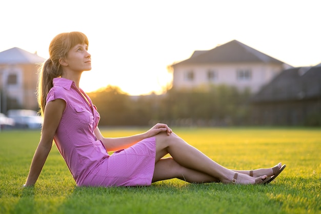 side view of young cute woman sitting on grass in good weather.