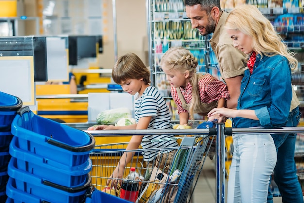 side view of young family with shopping cart full of purchases in supermarket