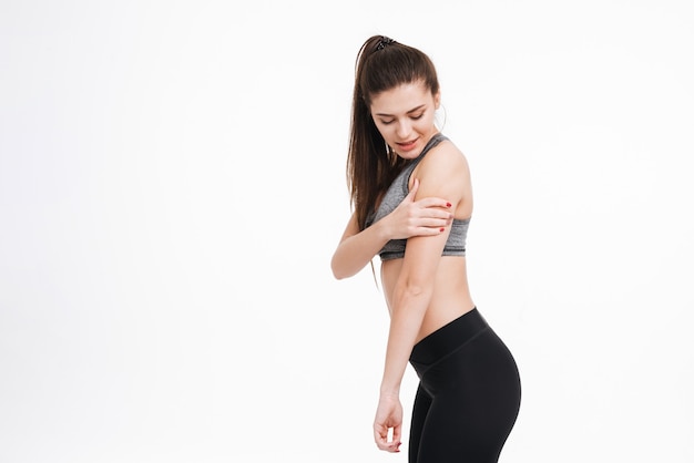 Side view of a young fitness woman in pain holding her arm and looking away isolated 