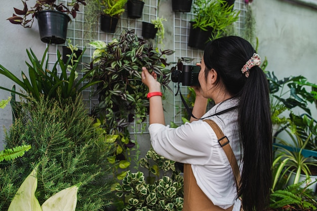 Foto vista laterale, la giovane donna giardiniera usa la fotocamera digitale per scattare una foto con una bella pianta d'appartamento