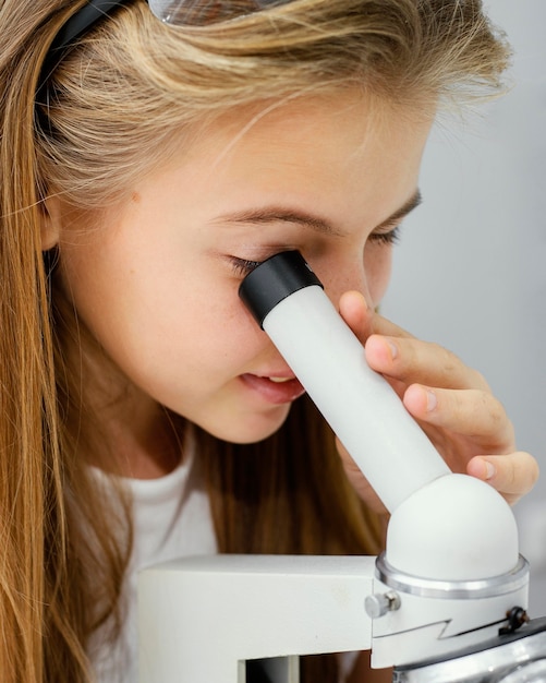 Foto vista laterale della giovane ragazza scienziato guardando attraverso il microscopio