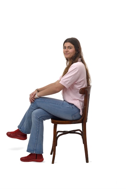 Photo side view of a young girl sitting on chair with cross legged and looking at camera on white background