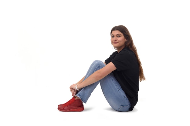 Photo side view of a young girl sitting on the floor looking at camera on white background