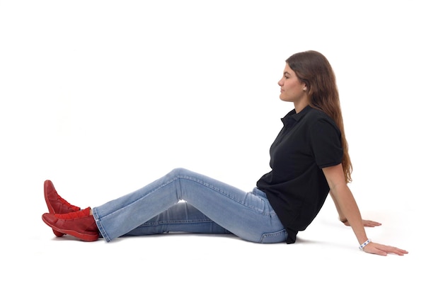 Photo side view of a young girl sitting on the floor with straight legs on white background