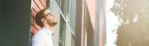 Side view of a young happy businessman listening to music with wireless earphones and mobile phone