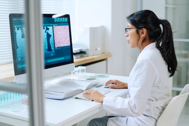 Side view of young hispanic female scientist studying new virus in laboratory