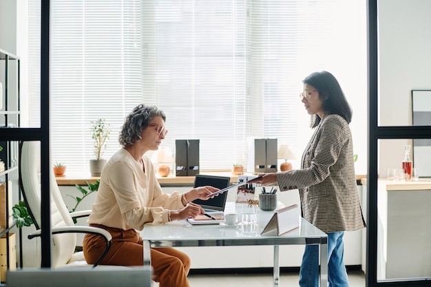 Side view of young hispanic female white collar worker passing document to boss