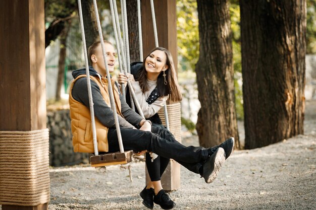 Photo side view of young loving couple sitting on swing in park outdoors