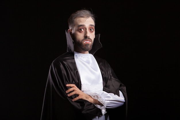 Side view of young man dressed up like a vampire looking curious into the camera. Dracula keeping his arms crossed.