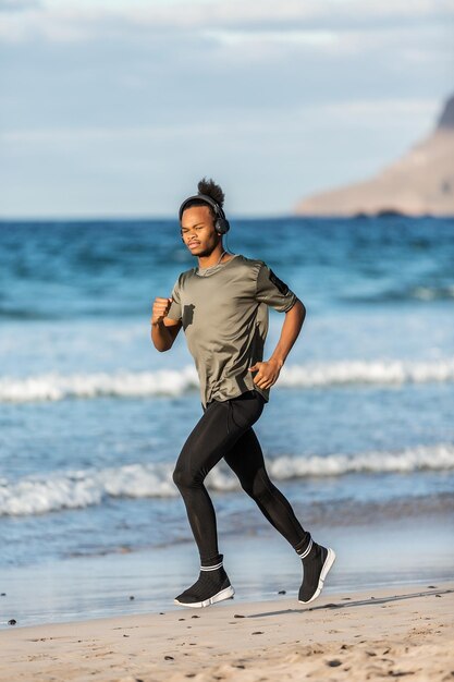 Photo side view of young man listening music while running at beach