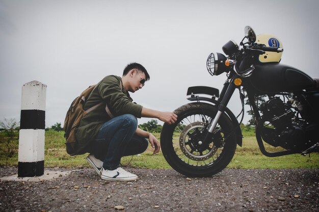 Photo side view of young man looking at tire of motorcycle