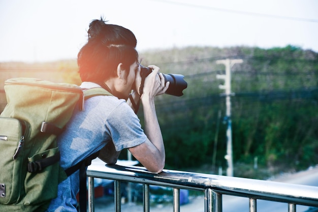 Side view of young man photographing while standing by railing against sky