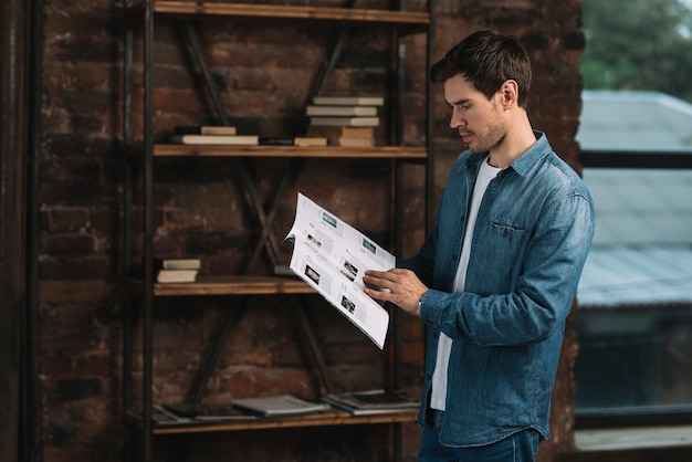 Вид сбоку молодой человек, читающий журнал дома