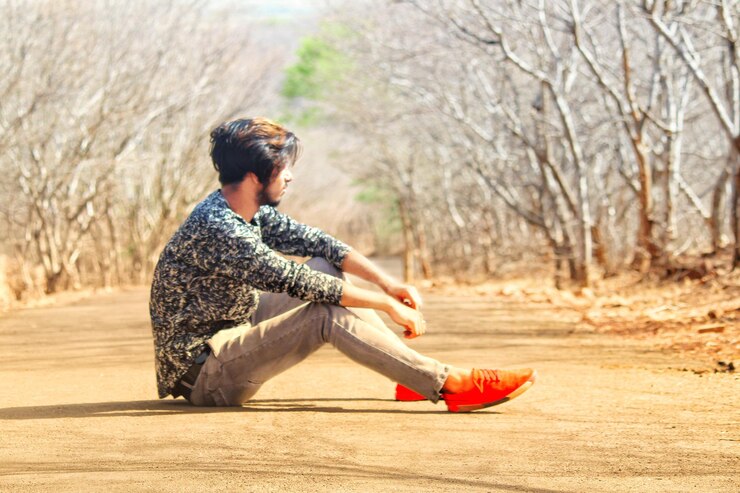 फोटो side view of young man sitting on footpath amidst bare trees