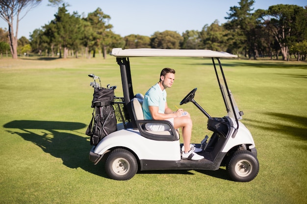 Side view of young man sitting in golf buggy