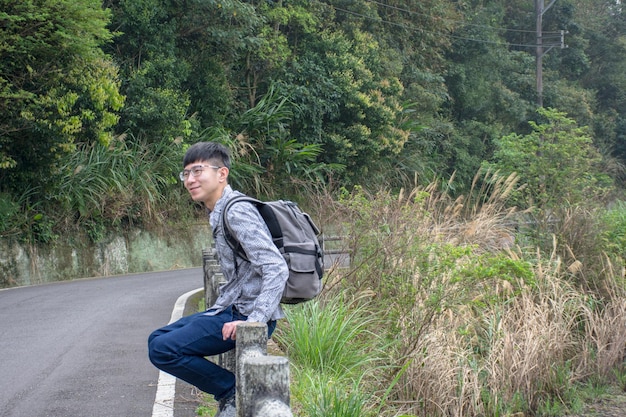 Side view of young man sitting on railing against trees