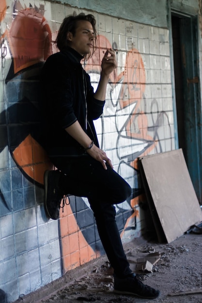 Foto vista laterale di un giovane che fuma una sigaretta mentre si trova accanto al muro