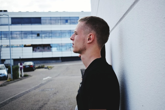 Foto vista laterale di un giovane in piedi contro un muro bianco