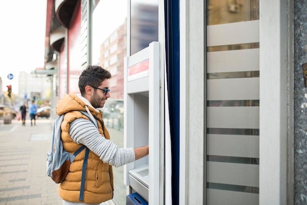 Photo side view of young man using atm in city