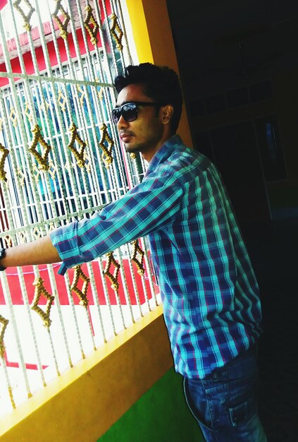 Side view of young man wearing sunglasses looking through window at home