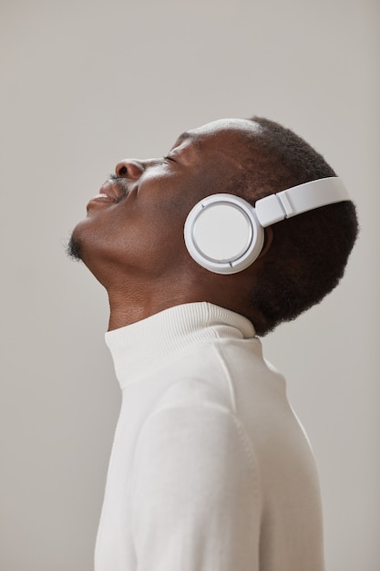 灰色の壁に分離された音楽を楽しんでいるワイヤレスヘッドフォンで若い男の側面図