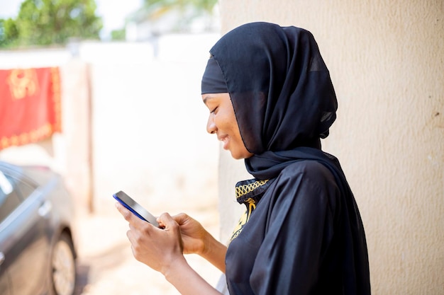 Side view of a young Nigerian muslim woman chatting on her smartphone