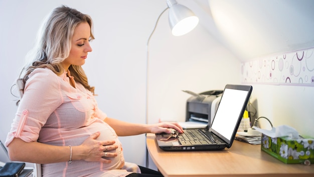 Foto vista laterale della giovane donna incinta che per mezzo del computer portatile alla notte