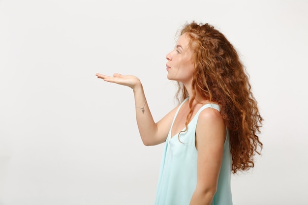 Side view of young redhead woman girl in casual light clothes posing isolated on white background in studio. People sincere emotions lifestyle concept. Mock up copy space. Blowing sending air kiss.