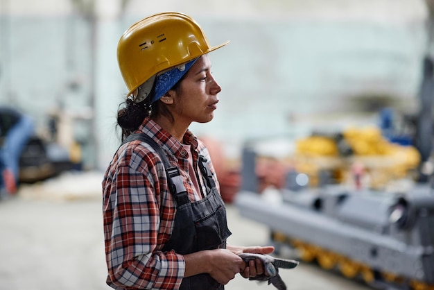 Photo side view of young tired female worker of factory in hardhat and coveralls