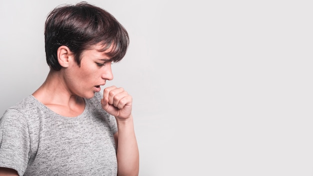 Photo side view of young woman coughing against gray background