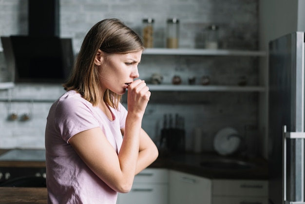 Side view of a young woman coughing at home