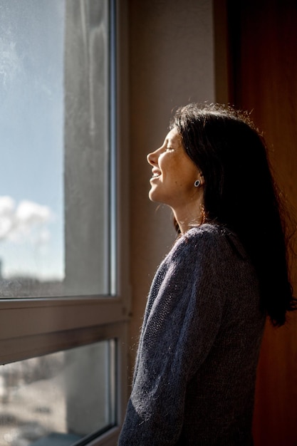 Photo side view of young woman looking through window