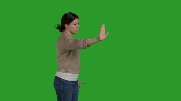 Photo side view of young woman raising palm as rejection gesture, expressing disapproval and disagreement symbol. female model showing stop talking sign with hand, refuse and reject on greenscreen.