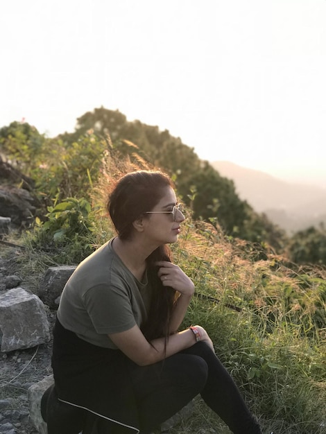 Photo side view of young woman sitting at mountain peak during sunset