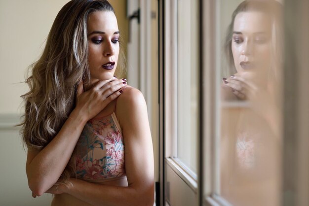 Photo side view of young woman standing by window at home